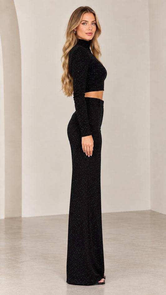 Side profile of model wearing black sparkle long sleeve crop top and high waist wide leg pants